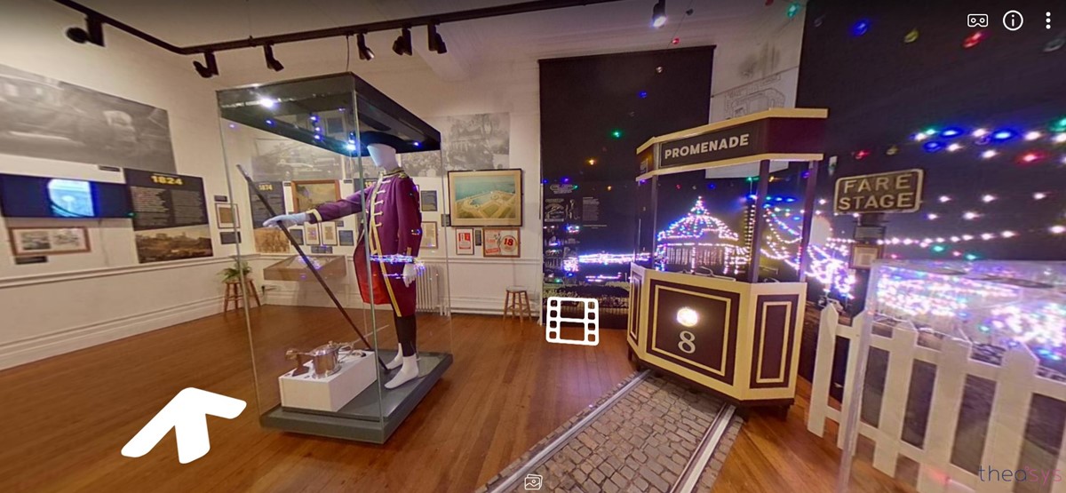 Screenshot from the Corporation Street virtual exhibition. Parts of the display include: a mock-up of a tram on Morecambe Promenade, surrounded by coloured lights to represent the illuminations. A frock coat and tricorn hat once worn by the mayor. Various information panels with symbols indication links to videos, text and images that can be accessed through the virtual tour.